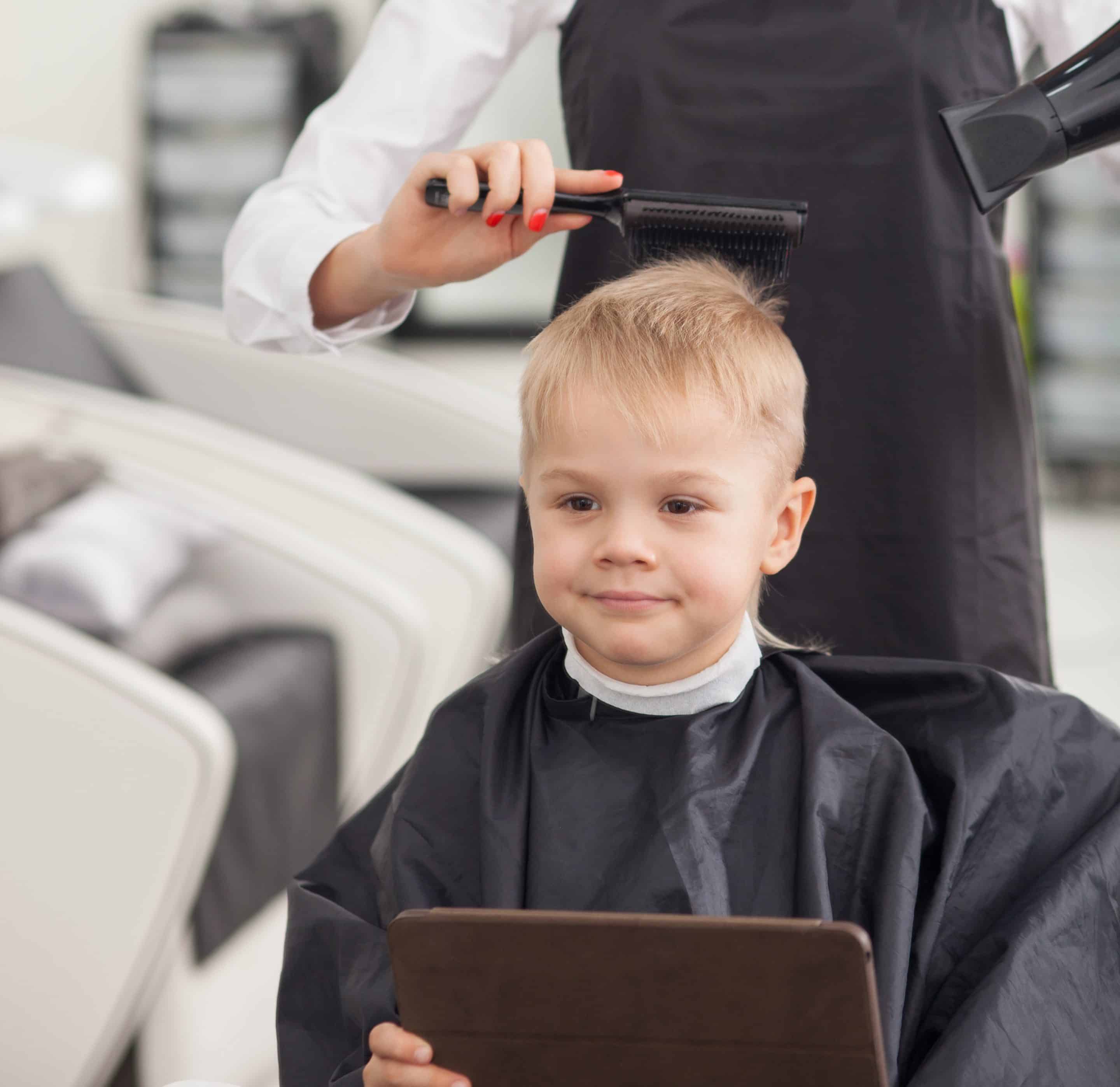 Nuori poika istuu parturissa hiusten leikkuussa